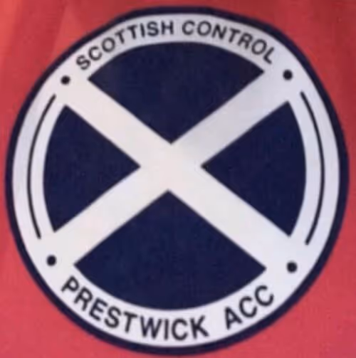 Round emblem with a white Saint Andrew's cross on a navy blue background, encircled by the text 'Scottish Control Prestwick ACC' on a white border.